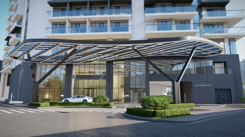 Entrée d&#039;un immeuble d&#039;appartements moderne à Dubaï avec un élégant auvent métallique incurvé, une verdure paysagée de chaque côté et une voiture blanche garée devant. Le bâtiment dispose de grandes portes et fenêtres vitrées.