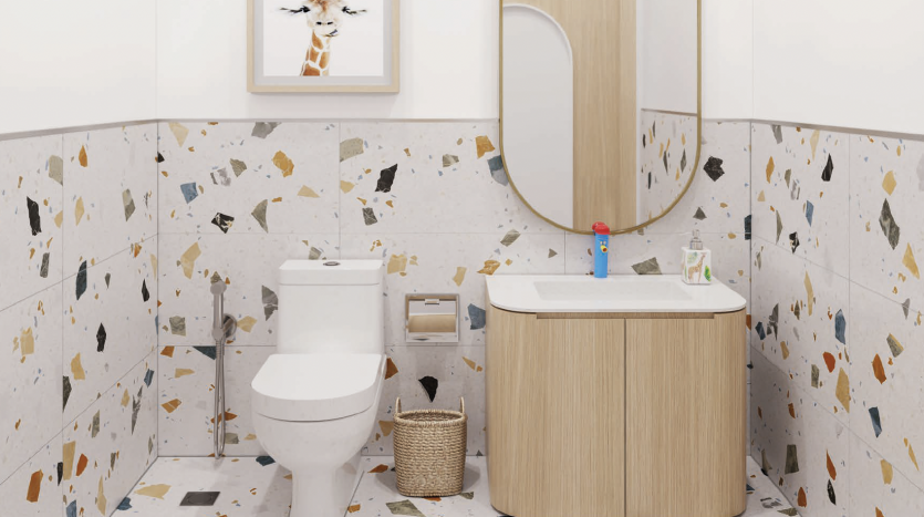 Une salle de bains moderne avec un mur carrelé en terrazzo avec des taches colorées, équipée de toilettes blanches, d&#039;une vanité en bois surmontée d&#039;un miroir ovale et d&#039;un petit panier en osier. UN
