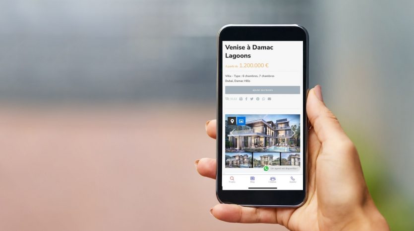 Main d&#039;une personne tenant un smartphone affichant une application immobilière avec une annonce pour &quot;Les Lagons de Venise à Damac&quot; au prix de 1 200 000 €, avec des images de bâtiments modernes.
