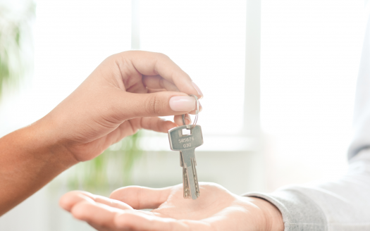 Une personne remet un jeu de clés à la main tendue d'une autre personne, suggérant un transfert de propriété d'un appartement à Dubaï, avec une fenêtre lumineuse en arrière-plan.