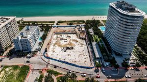 Vue aérienne d'un chantier de construction côtier flanqué d'un immeuble de grande hauteur et d'une plage à Dubaï, montrant un développement en cours, entouré de rues et de structures adjacentes.