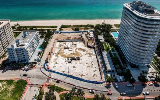 Vue aérienne d'un chantier de construction côtier flanqué d'un immeuble de grande hauteur et d'une plage à Dubaï, montrant un développement en cours, entouré de rues et de structures adjacentes.