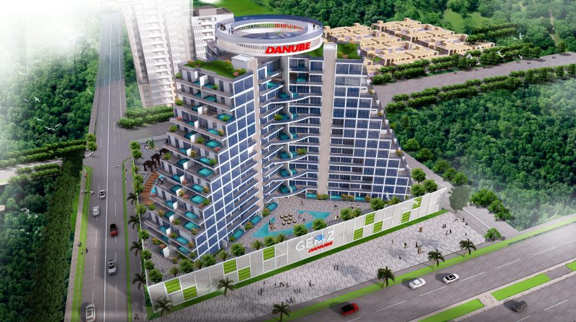 Vue aérienne d&#039;un immeuble d&#039;appartements moderne à plusieurs étages à Dubaï avec des balcons en verre teinté bleu, entouré d&#039;une verdure luxuriante et adjacent à une rue avec des voitures en mouvement. Le bâtiment présente des caractéristiques proéminentes