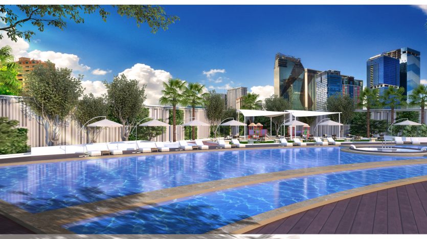 Espace piscine luxueux avec chaises longues et parasols, entouré d&#039;arbres tropicaux et d&#039;immeubles modernes de grande hauteur sous un ciel bleu clair, disponible via notre agenceimmobilière Dubaï.