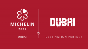 Immagine promozionale di una partnership per la Guida Michelin 2022 con Villa Dubai come destinazione partner. I loghi Michelin e Dubai sono evidenziati su uno sfondo rosso.