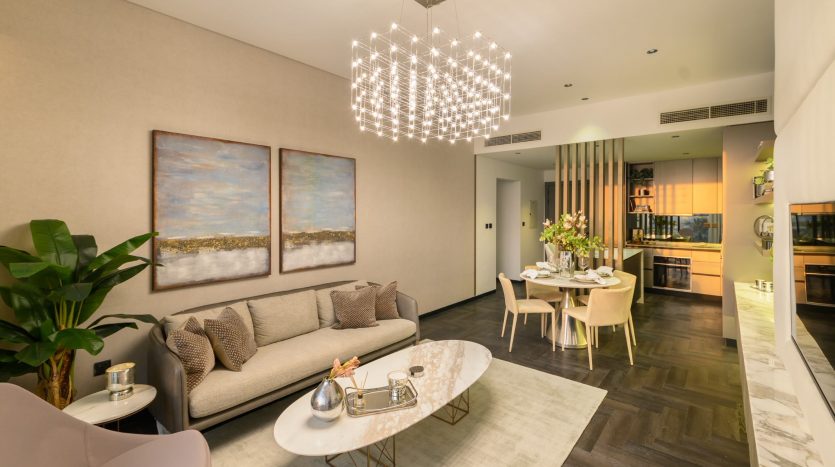 Villa moderne à Dubaï avec un canapé beige, une table basse en marbre et des chaises pastel. Deux tableaux de paysages sont suspendus au-dessus du canapé et un lustre illumine l&#039;espace. Une cuisine ouverte est visible