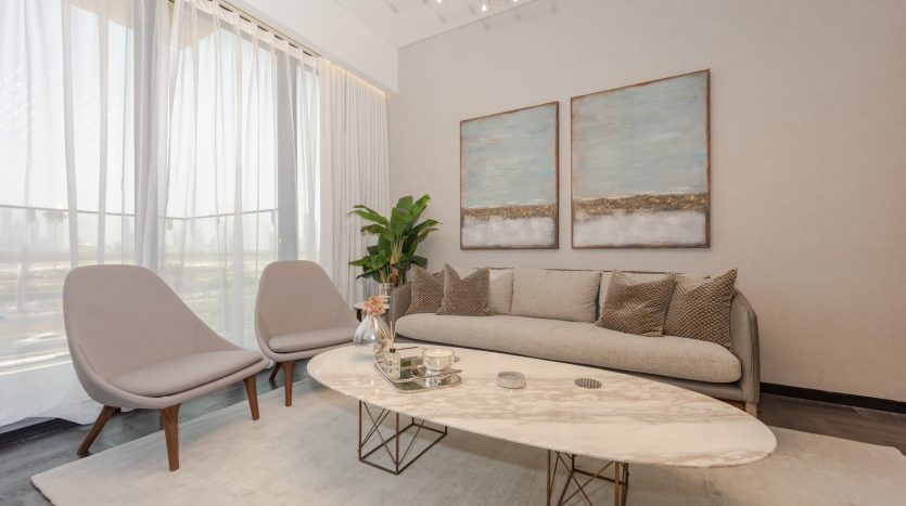 Un salon moderne et lumineux dans une villa à Dubaï, comprenant un canapé beige avec des oreillers, deux chaises grises, une grande table basse ovale en marbre, des peintures abstraites bleues et dorées au mur,