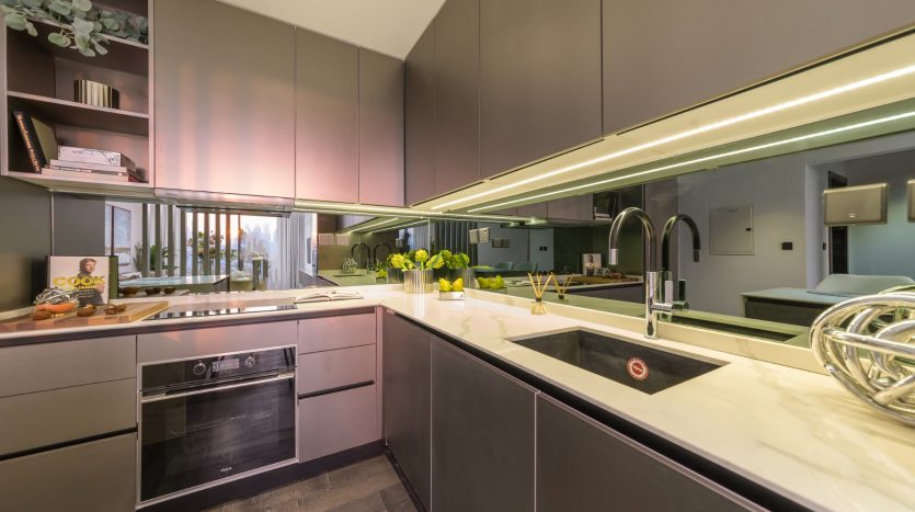 Intérieur de cuisine moderne avec armoires grises élégantes, comptoirs en marbre et appareils électroménagers intégrés. Les surfaces réfléchissantes et l&#039;éclairage ambiant créent une sensation lumineuse et spacieuse dans cette villa de Dubaï.