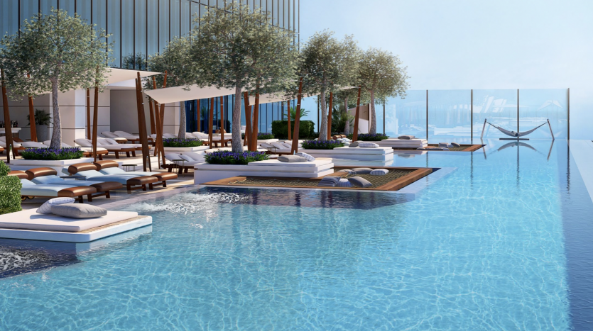 Une luxueuse piscine à débordement sur le toit avec de l&#039;eau bleu clair, entourée d&#039;arbres, de chaises longues et de cabanes, donnant sur une vue panoramique sur l&#039;océan depuis un emplacement prestigieux de l&#039;immobilier de Dubaï.