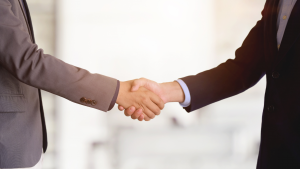 Due persone in abiti da lavoro si stringono la mano in un appartamento di Dubai, con uno sfondo sfocato di un ufficio. Il gesto simboleggia un accordo o un saluto professionale.