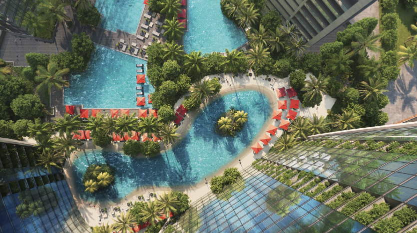 Vue aérienne d&#039;un luxueux complexe tropical à Dubaï avec des piscines sinueuses bordées de palmiers, des chaises longues rouges et une structure au toit de verre à proximité d&#039;une verdure luxuriante.