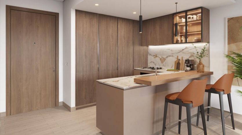 Intérieur de cuisine moderne comprenant un îlot central avec des tabourets de bar, des armoires en bois, des suspensions et des appareils intégrés, le tout dans un agencement lumineux et minimaliste dans un appartement de Dubaï.