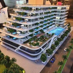 Modello di un moderno appartamento multipiano a Dubai con terrazze e piscine, circondato da alberi e piccole figure che rappresentano persone e automobili.