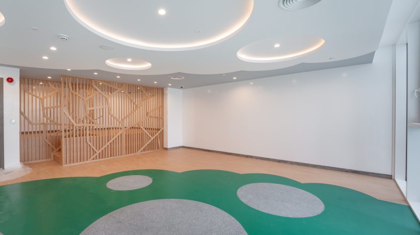 Intérieur moderne et spacieux d&#039;une aire de jeux pour enfants avec cloison en treillis de bois, tapis verts circulaires au sol et grands luminaires circulaires au plafond dans un emplacement privilégié de Dubaï.