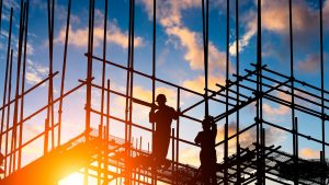 Silhouettes d'ouvriers du bâtiment sur des échafaudages contre un ciel coucher de soleil vibrant, représentant un chantier de construction actif à Dubaï.