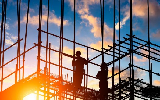 Silhouettes d'ouvriers du bâtiment sur des échafaudages contre un ciel coucher de soleil vibrant, représentant un chantier de construction actif à Dubaï.