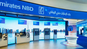 Intérieur d'une succursale bancaire Emirates NBD dans une villa de Dubaï avec plusieurs guichets automatiques, un service d'assistance et des affichages promotionnels sous une signalisation bleue et blanche bien éclairée.