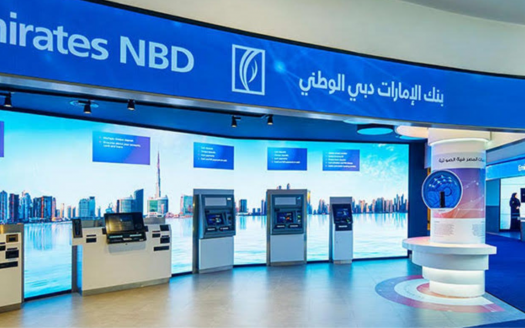 Intérieur d'une succursale bancaire Emirates NBD dans une villa de Dubaï avec plusieurs guichets automatiques, un service d'assistance et des affichages promotionnels sous une signalisation bleue et blanche bien éclairée.