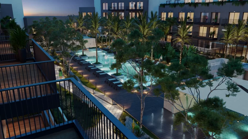 Vue nocturne d&#039;un luxueux balcon d&#039;hôtel donnant sur une piscine éclairée entourée de palmiers, avec des façades de bâtiments modernes en arrière-plan à Dubaï.