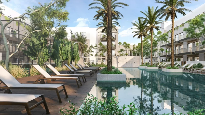 Piscine luxueuse du complexe entourée de palmiers luxuriants et de bâtiments modernes à Dubaï, avec des chaises longues et des plantes vertes se reflétant dans l&#039;eau calme.
