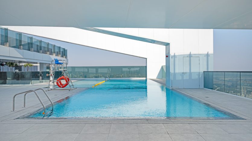 Une piscine moderne sur le toit d&#039;une villa de Dubaï au design élégant et minimaliste, avec une eau bleu clair, entourée d&#039;une terrasse blanche et de barrières de verre, sous un ciel clair et lumineux.