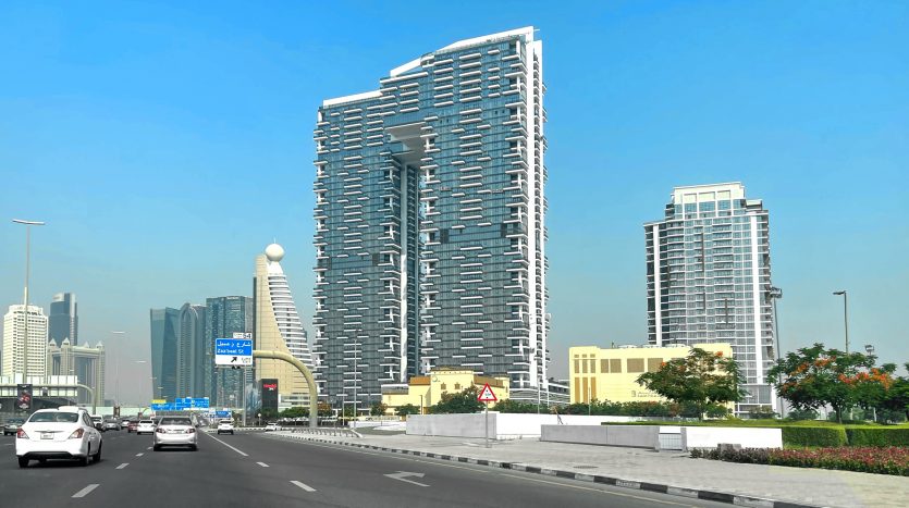 Une rue animée de Dubaï avec des gratte-ciel modernes sous un ciel bleu clair. Les voitures roulent sur la route et un gratte-ciel unique et sinueux domine l&#039;horizon.