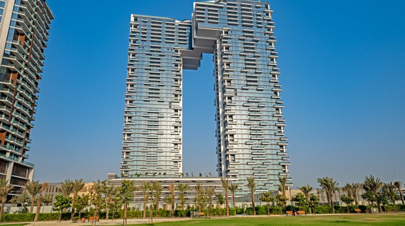 Immeuble d&#039;appartements architectural moderne à Dubaï avec un design unique en forme de U, entouré de parcs verdoyants et d&#039;un ciel bleu clair.