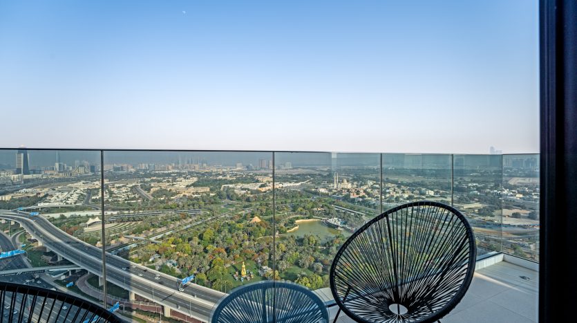 Une vue panoramique de Dubaï depuis un balcon en hauteur, doté de deux chaises et d&#039;une balustrade en verre qui surplombe un vaste paysage de routes et d&#039;espaces verts.