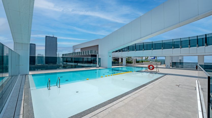 Une piscine moderne sur le toit entourée de barrières de verre et de bâtiments blancs élégants sous un ciel bleu clair, avec des gratte-ciel visibles en arrière-plan. Ce cadre haut de gamme est une opportunité d&#039;investissement idéale à Dubaï