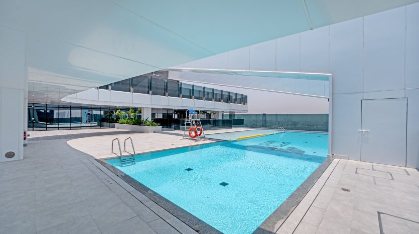Une piscine extérieure sur un toit au design moderne et minimaliste avec des lignes épurées et une eau bleu clair. La zone, qui fait partie d&#039;un projet d&#039;investissement Dubaï, est entourée de barrières de verre et possède une