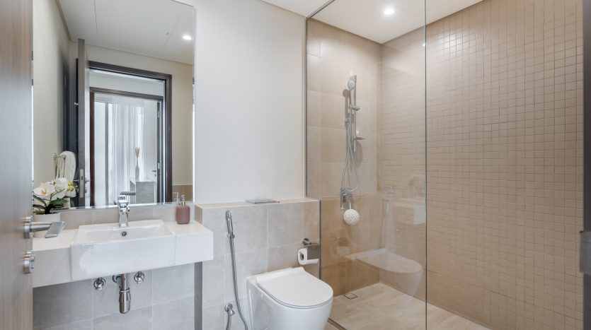Intérieur de salle de bains de villa moderne à Dubaï avec double vasque, grand miroir, toilettes et douche à l&#039;italienne entourée de portes en verre. Conception de carrelage neutre avec lumière naturelle.