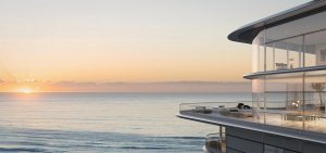 Une maison de luxe moderne à la façade vitrée surplombant l'océan au coucher du soleil, avec un ciel clair et une mer calme, idéale pour un investissement sur le marché immobilier de Dubaï.