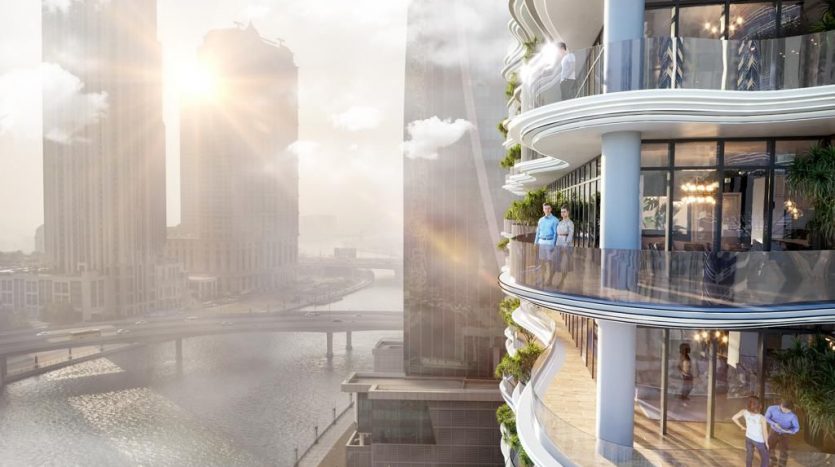 Une terrasse extérieure sereine et ensoleillée d&#039;un appartement de grande hauteur à Dubaï surplombant la rivière d&#039;une ville et d&#039;autres gratte-ciel, avec des personnes profitant de la vue.