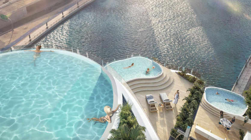 Vue aérienne de deux piscines extérieures à débordement surplombant une rivière calme. Les gens nagent et se prélassent au bord de la piscine, se prélassant au soleil de Dubaï.