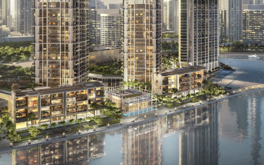 Vue aérienne d'un développement moderne en bord de mer avec plusieurs appartements de grande hauteur, des espaces verts luxuriants et des façades éclairées au crépuscule dans un cadre urbain à Dubaï.