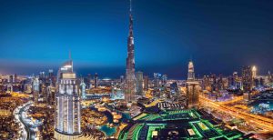 Une vue panoramique nocturne de Dubaï mettant en valeur l'horizon illuminé avec le Burj Khalifa dominant les gratte-ciel environnants, les voies navigables éclairées et les appartements luxueux.