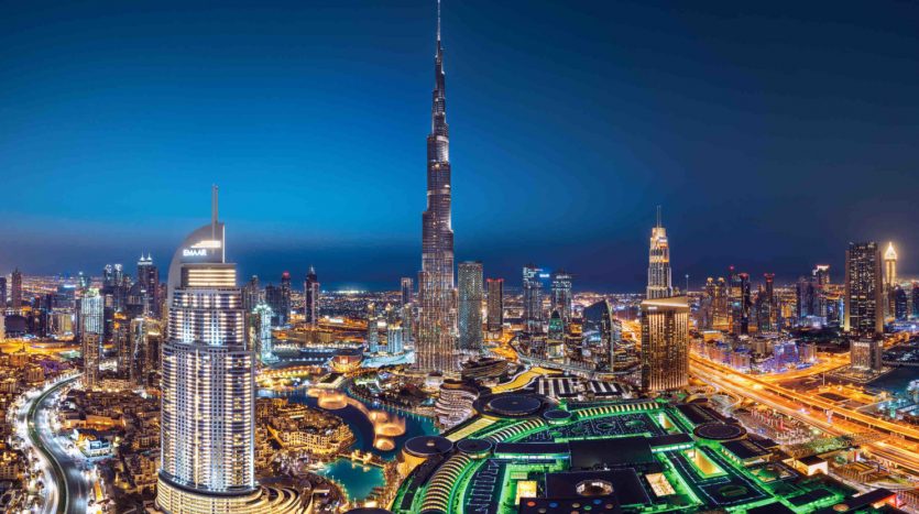 Une vue panoramique nocturne de Dubaï mettant en valeur l&#039;horizon illuminé avec le Burj Khalifa dominant les gratte-ciel environnants, les voies navigables éclairées et les appartements luxueux.