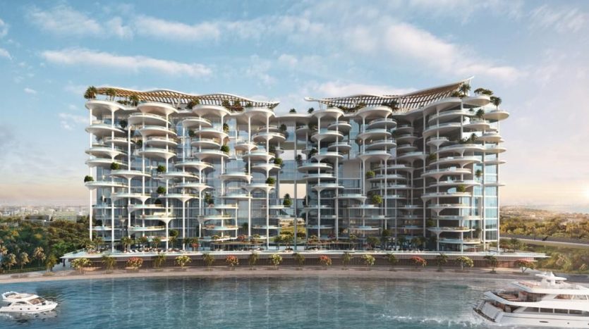 Un immeuble d&#039;appartements moderne et luxueux en bord de mer à Dubaï avec plusieurs balcons, de vastes façades en verre et surmonté de toits verts. Plusieurs yachts sont amarrés à proximité dans un plan d’eau bleu clair.