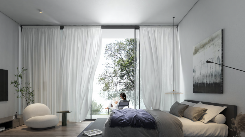 Une chambre moderne dans un appartement de Dubaï avec de grandes fenêtres couvertes de rideaux blancs, offrant une vue sur les arbres. L&#039;intérieur comprend un lit, des œuvres d&#039;art, une télévision et une chaise avec une personne lisant