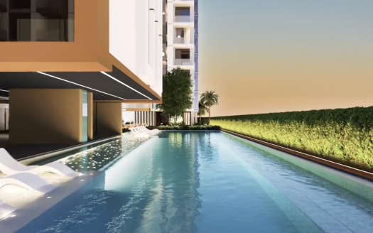 Une piscine extérieure à côté de bâtiments résidentiels modernes à Dubaï au crépuscule, avec une eau bleu clair, des chaises longues blanches au bord de la piscine et une haie soigneusement taillée.