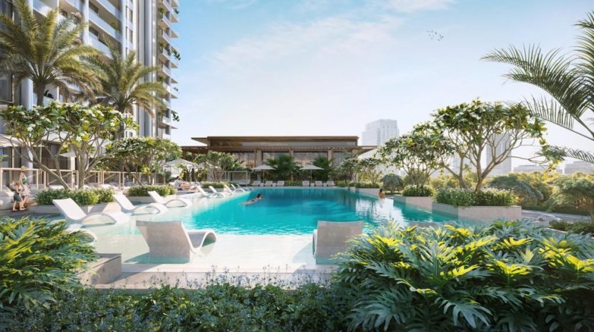 Un espace piscine luxueux entouré d&#039;une verdure luxuriante avec des chaises longues et un bar au bord de la piscine, ombragé par un immeuble de grande hauteur, illustre l&#039;immobilier de premier choix à Dubaï. Les gens se détendent et nagent dans le