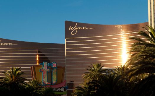 Vue des hôtels Encore et Wynn de Las Vegas, avec leurs façades marron brillantes éclairées par le soleil, et des palmiers au premier plan sous un ciel bleu clair.