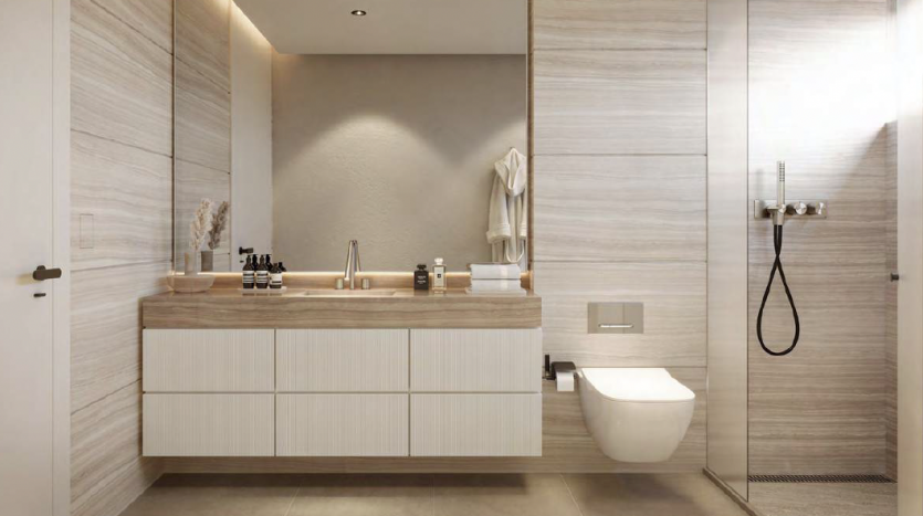 Salle de bain moderne comprenant une grande vanité avec des armoires blanches et des accents de bois, des toilettes murales et une cabine de douche en verre. Des tons neutres et des lignes épurées dominent l&#039;espace de cet appartement de Dubaï.