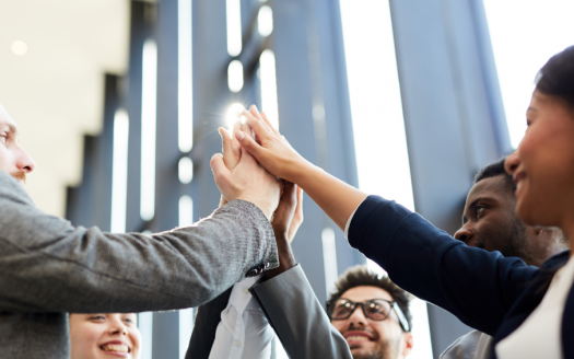 Un groupe diversifié de cinq collègues de travail se donnant un high five en cercle, exprimant le travail d'équipe et le succès dans le cadre d'une villa moderne à Dubaï.