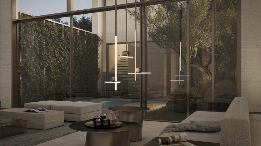 Un salon moderne avec des baies vitrées donnant sur une cour sereine. La pièce présente un design minimaliste avec des tons neutres et comprend des meubles et des suspensions chics et contemporains, parfaits comme investissement à Dubaï.