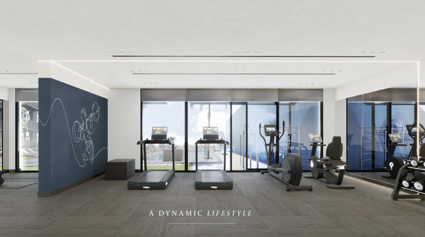 Une salle de sport spacieuse et moderne dans un appartement de Dubaï avec de grandes fenêtres offrant une vue sur la montagne. La salle dispose de tapis roulants, de vélos d&#039;exercice et de machines elliptiques. Le sol est carrelé et il y a