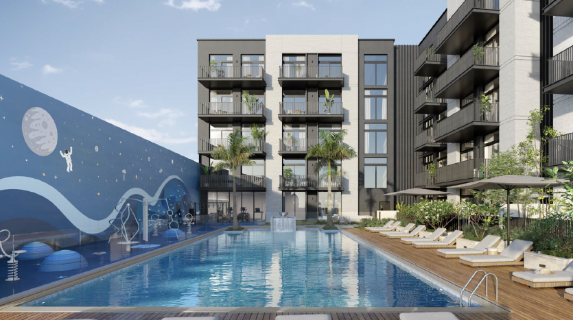 Un immeuble d&#039;appartements moderne à Dubaï avec des balcons donnant sur une grande piscine flanquée de chaises longues sous un ciel bleu clair. Une fresque murale représentant une pieuvre sur un mur ajoute une touche ludique.