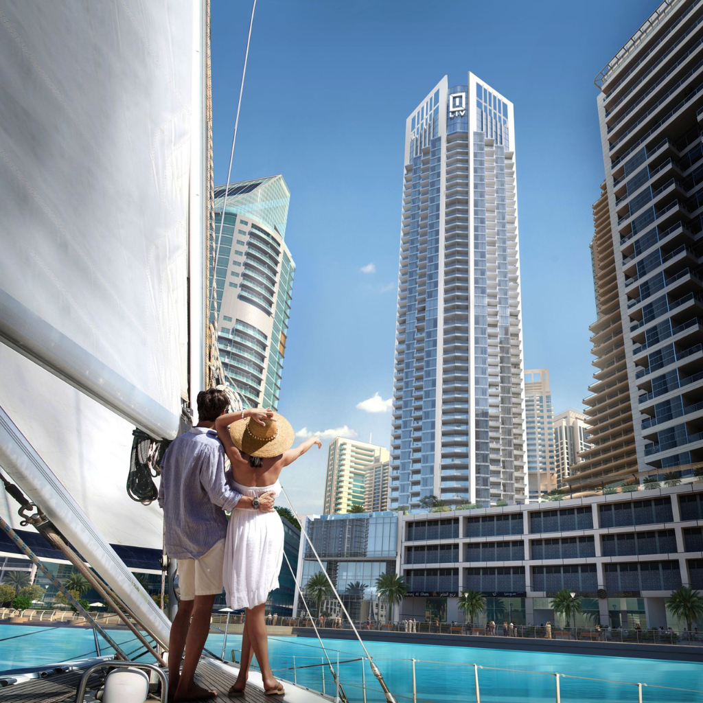 Un couple se tient rapproché sur un yacht, s'embrassant tout en regardant les gratte-ciel modernes au bord d'un front de mer bleu clair à Dubaï, sous un ciel ensoleillé.