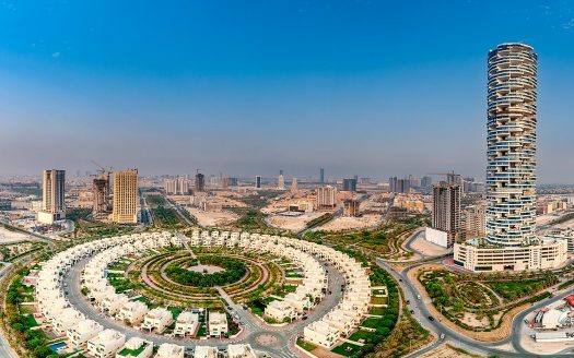 Une vue panoramique d'un paysage urbain moderne présentant des aménagements résidentiels incurvés et une tour de grande hauteur à Dubaï. Les chantiers de développement et de construction de banlieue s'étendent à l'horizon sous un ciel dégagé.