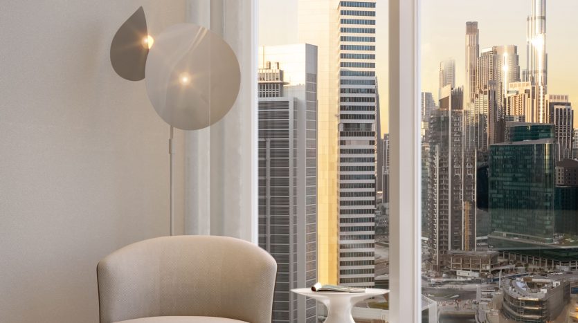 Un coin moderne et confortable dans un appartement de grande hauteur à Dubaï, doté d&#039;une chaise et d&#039;une lampe élégantes avec une vue panoramique sur les toits animés de la ville au coucher du soleil.